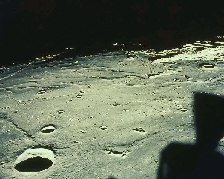 Moonscape,  
       with craters receding into inky distance. A shadow of the Command 
       Module glides over barren plains. (NASA photo)